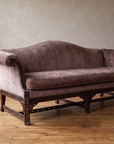 Mauve velvet Chinese Chippendale camelback sofa, front view, against a plaster wall on a reclaimed wood floor