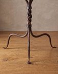 Three evenly spaced curved iron legs with pad feet on a reclaimed wood floor