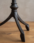 Close-up of the forged iron tripod base with three splayed legs and spade feet on a reclaimed wood floor