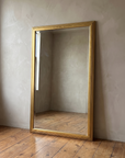 Gilt reeded wood mirror leaning against a warm plaster wall on a reclaimed wood floor