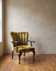 Vintage chartreuse crushed velvet channel-back armchair against a hand-troweled plaster wall on a reclaimed wood floor, three-quarter view