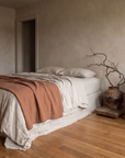 The cane barrel chair beside a linen-dressed bed, showing its compact size