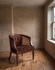 Three-quarter view of the cocoa velvet cane barrel chair in a quiet apartment corner by the window