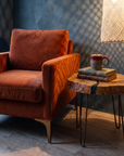 Close-up of the rust velvet arm and seat beside a wood slab side table in lattice lamplight