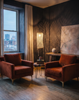 Pair of rust velvet armchairs in a dusky plaster room with a netted lamp and a soft abstract painting