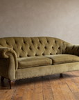 Ralph Lauren olive velvet button tufted sofa against a greige plaster wall on a reclaimed wood floor