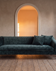 Tess sofa in a plaster room before an arched doorway glowing with late afternoon light, a side table with tea and books