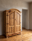 Handmade Mexican pine bonnet-top armoire against a greige plaster wall on a reclaimed wood floor