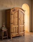 The armoire in a plaster room with amber light glowing through an arch, a stool with books and tea beside it