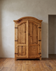 Front view of the pine armoire with arched crown, distressed doors and iron hinges