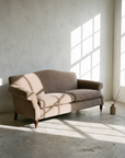 Taupe camelback sofa in a pale limewashed room with window light printing a grid across the wall