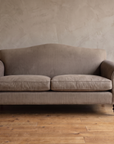 Front view of the taupe camelback sofa with both scroll arms and a pale stoneware vase of bare branches