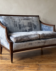 Ice blue velvet Directoire loveseat with mahogany frame, three-quarter view in a plaster-walled room