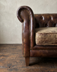 Close-up of the scroll arm, antique brass nailheads, crackled leather cushion and tapered leg