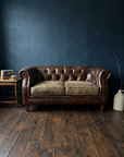 Leather chesterfield loveseat against a midnight blue plaster wall with a side table, books and tea