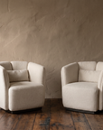 Two cream textile tub armchairs at a three-quarter angle in a plaster room with old wood floorboards