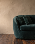 Close-up of the rounded arm and two ruched green velvet pillows on a curved sofa