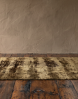 Low view along the length of the olive umber abstract rug showing its silken sheen