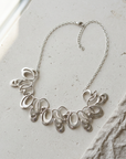Sterling silver statement necklace of many overlapping open loops, laid flat on pale stone