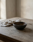 Dark charcoal hand thrown ceramic bowl with a bronze interior on a weathered wood table