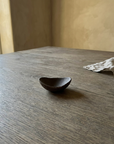 Small dark bronze hand thrown oval ceramic dish on a weathered wood table in soft daylight