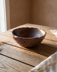 Terracotta hand thrown ceramic bowl with a torn uneven rim on a weathered wood table