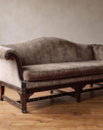 The Dorian, an antique carved Chinese Chippendale camelback sofa in taupe velvet, front view, against a plaster wall on a reclaimed wood floor