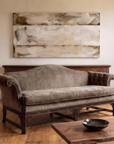 The Dorian taupe velvet camelback sofa floating in a calm limewash living room, antique console behind it, a large bone-and-umber abstract painting above, live-edge walnut coffee table in front