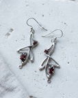Angular sterling silver Art Nouveau drop earrings set with garnets, laid flat on pale stone