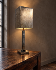 Mirrored column table lamp illuminated on a reclaimed wood console against taupe plaster
