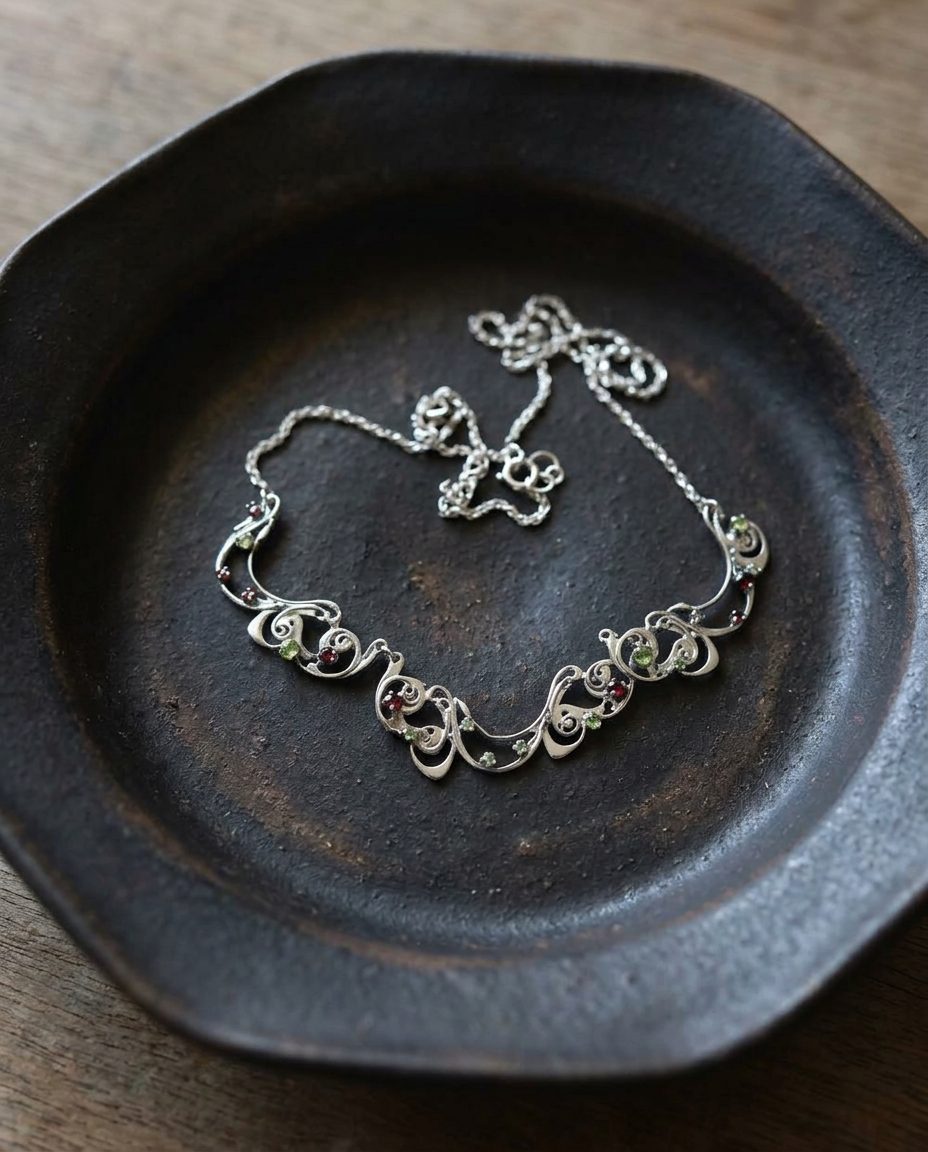 Garnet and Peridot Scroll Necklace on black ceramic dish