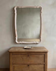 Blush French Provincial style mirror hung on a greige plaster wall above an antique wooden chest with a small ceramic dish