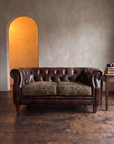 Leather chesterfield loveseat in a plaster salon with amber light through an arched doorway