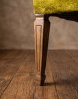 Chartreuse velvet diamond-tufted armchair, full-length macro of one front leg from seat to floor showing fluted carving and cap foot