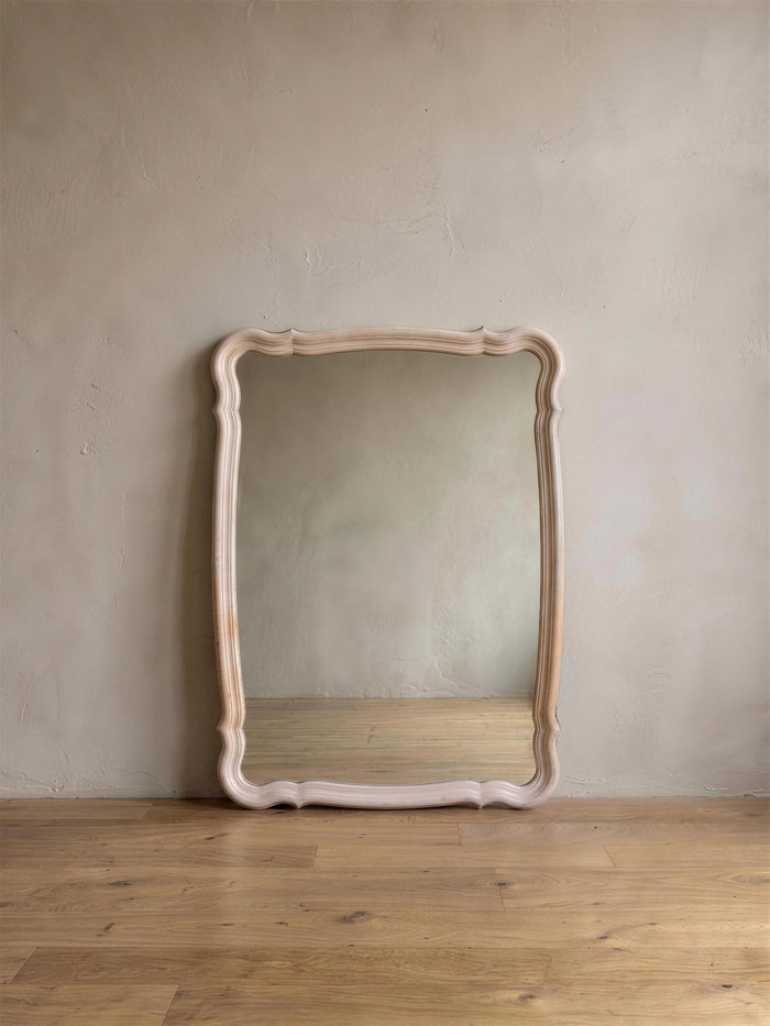 Blush French Provincial style mirror leaning against a greige plaster wall on a reclaimed wood floor