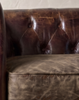 Close-up of the deep diamond button tufting above a crackled smoky brown leather cushion