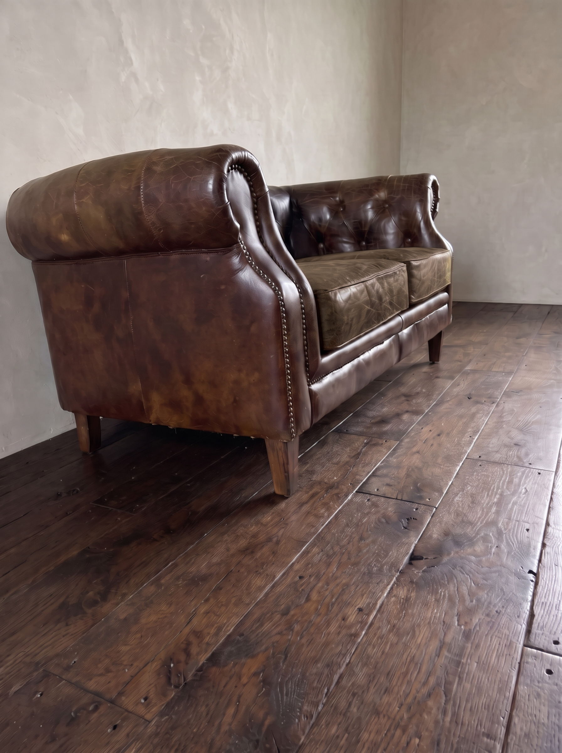 Low three-quarter view from the end of the leather chesterfield loveseat showing the arm roll and mottled patina
