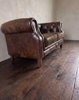 Low three-quarter view from the end of the leather chesterfield loveseat showing the arm roll and mottled patina