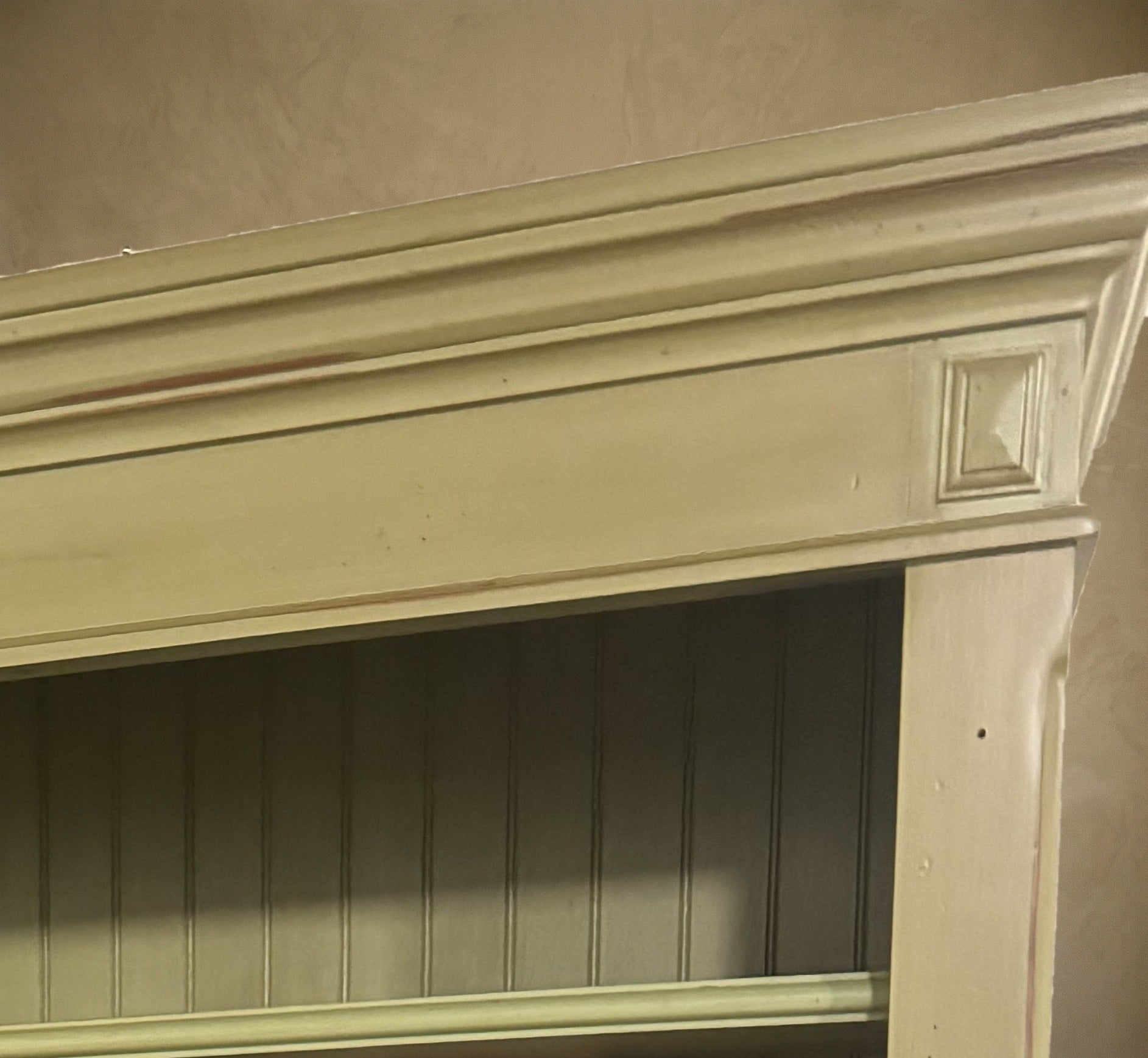 Close-up of the stepped cornice, square corner block and beadboard back in glazed olive green paint