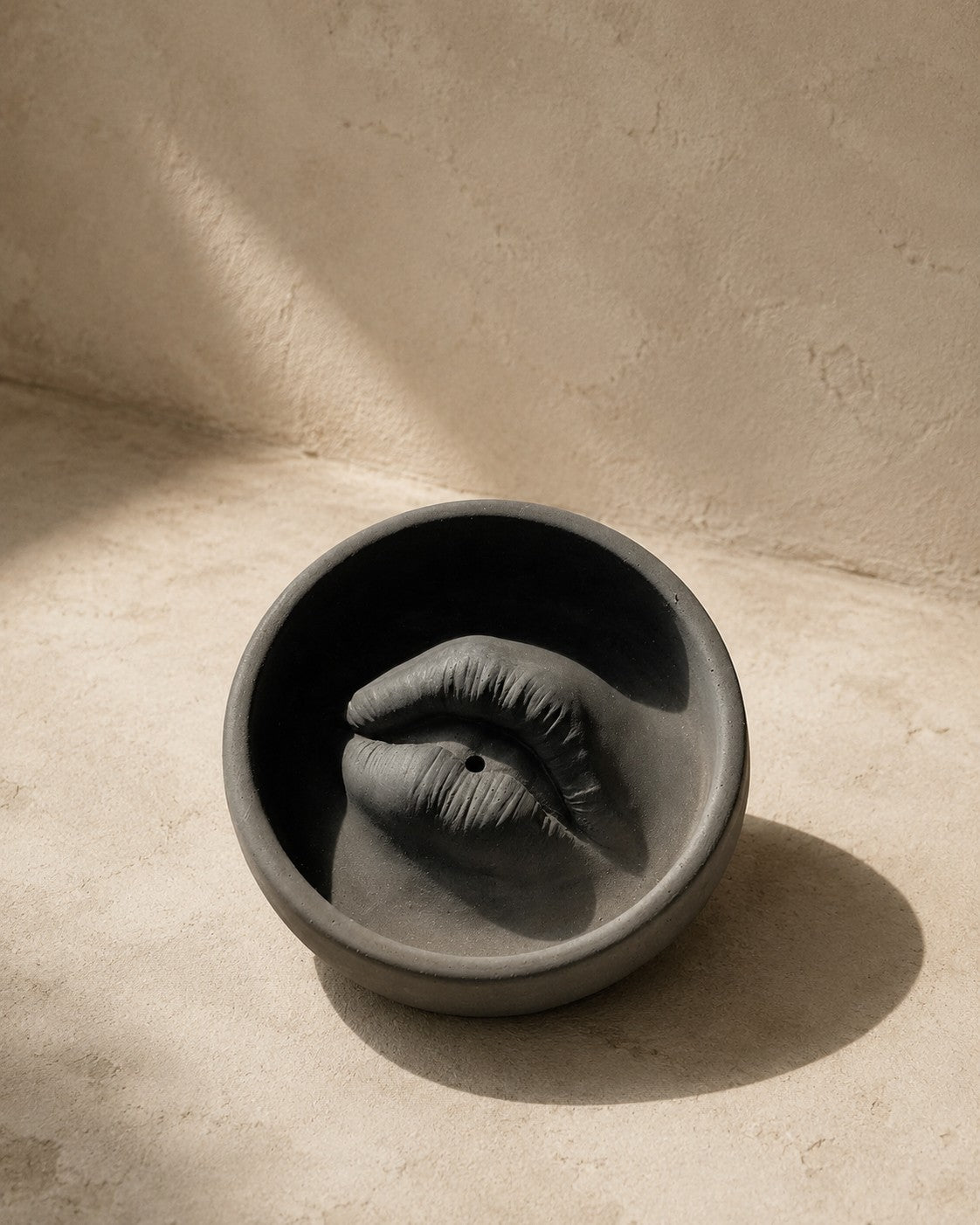 Lip Incense Holder in coal concrete, a lips form set in a round dish, on travertine