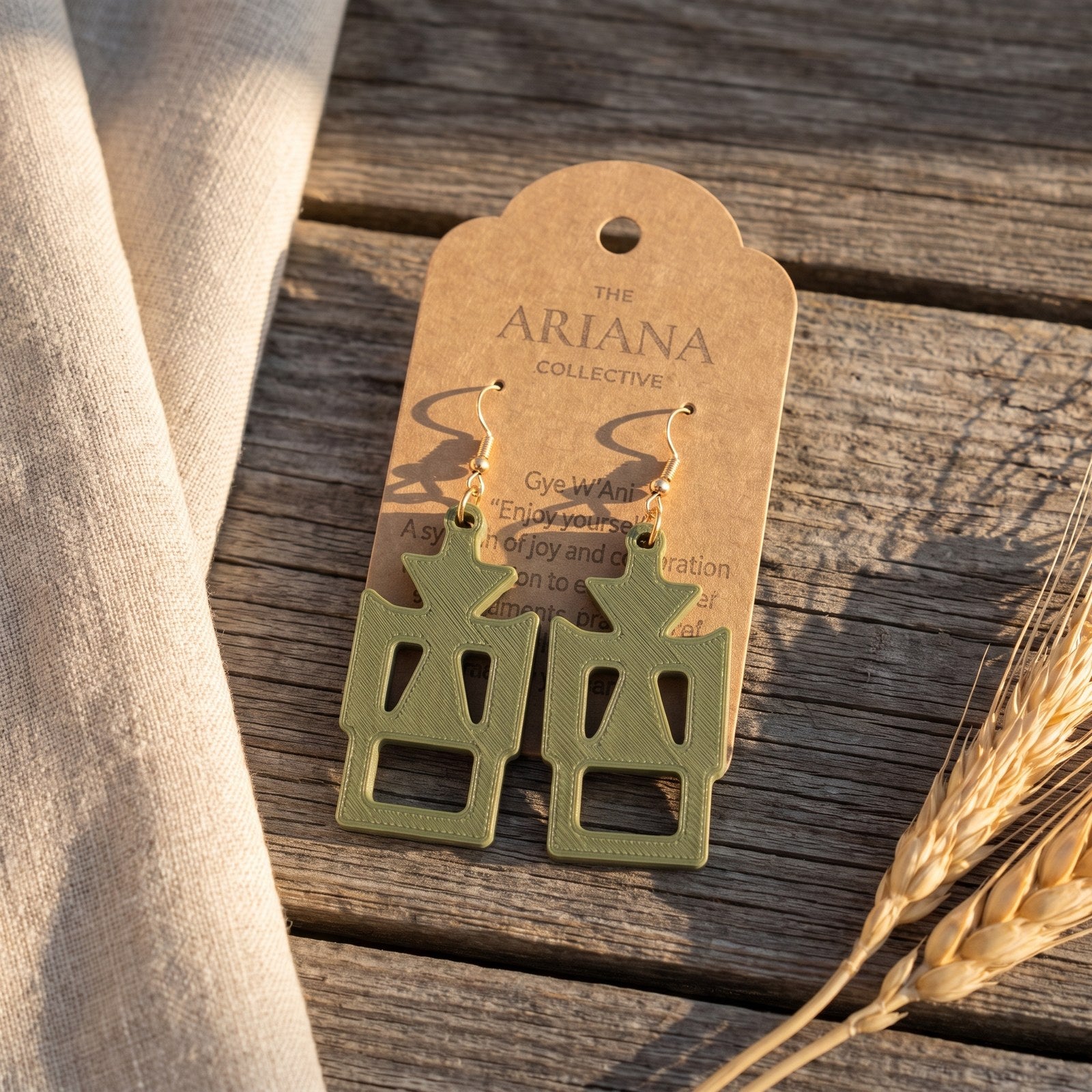 Gye W'Ani Adinkra earrings in olive green by The Ariana Collective, on a kraft tag