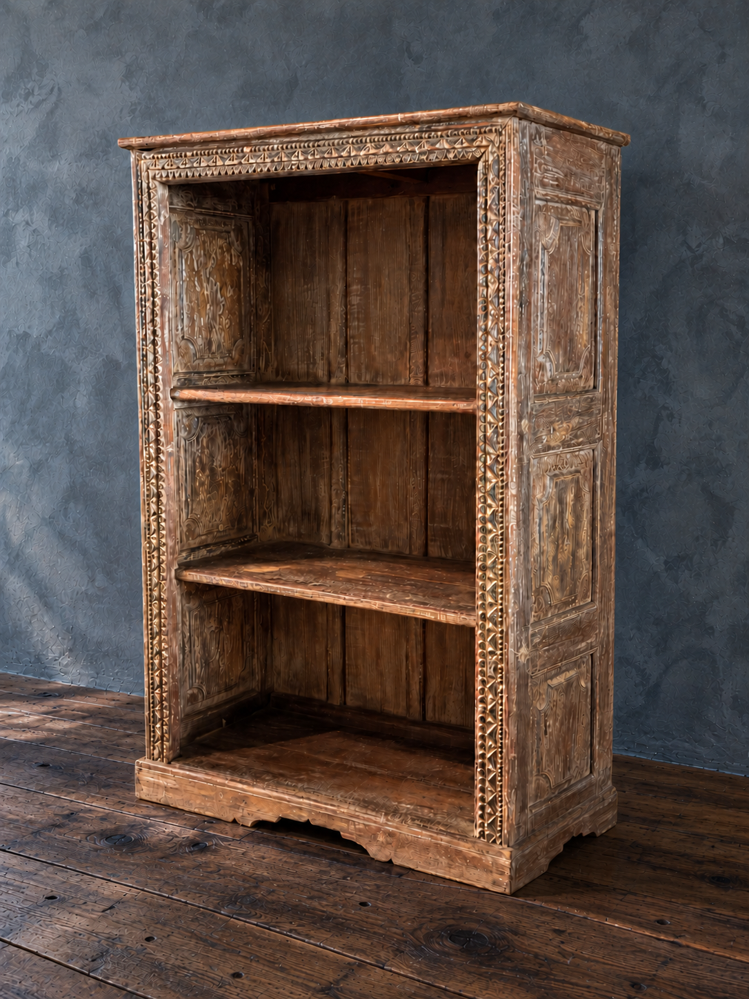 Carved wooden bookcase, bare, with paneled side and aged brown and pale finish.