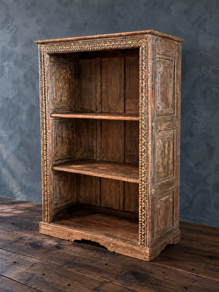 Carved wooden bookcase, bare, with paneled side and aged brown and pale finish.