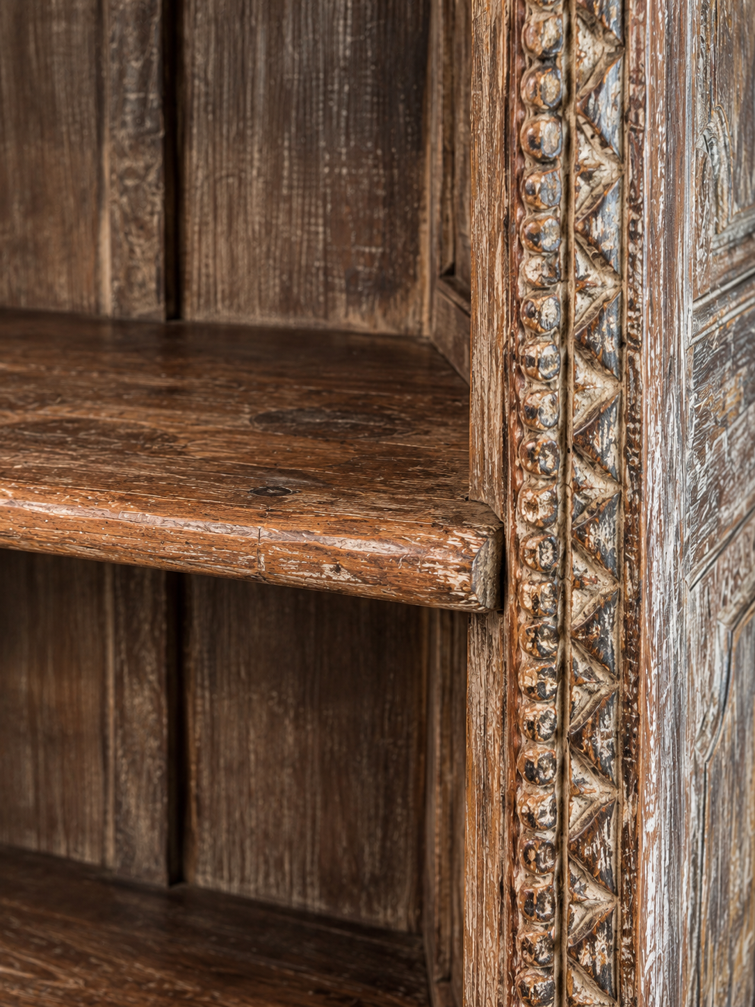 Shelf edge and carved upright showing aged wood and finish wear.