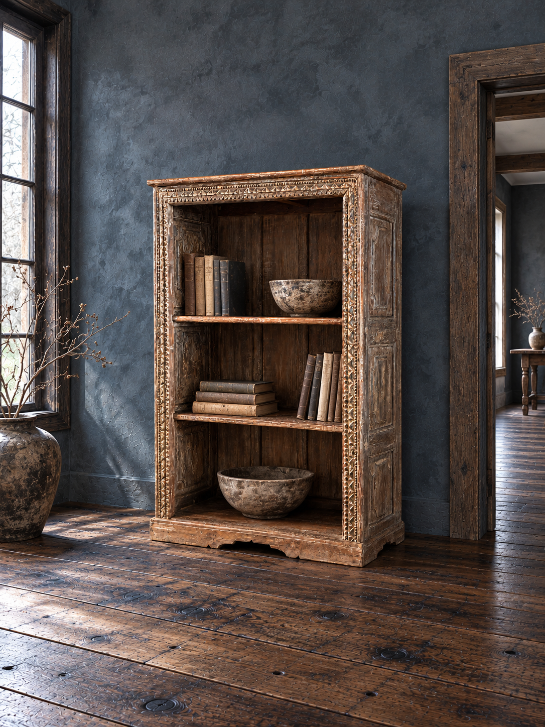 Carved bookcase beside a tall window on dark reclaimed wood flooring.