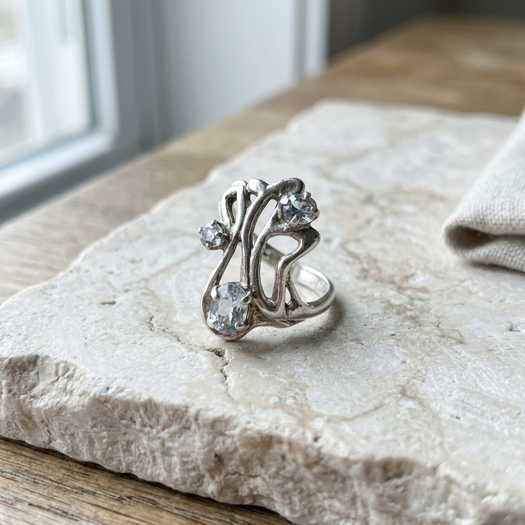 Sterling silver openwork ring with three clear stones, lying flat on pale limestone
