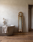 Gilt scroll mirror standing upright beside a stone soaking tub in a plaster bathroom