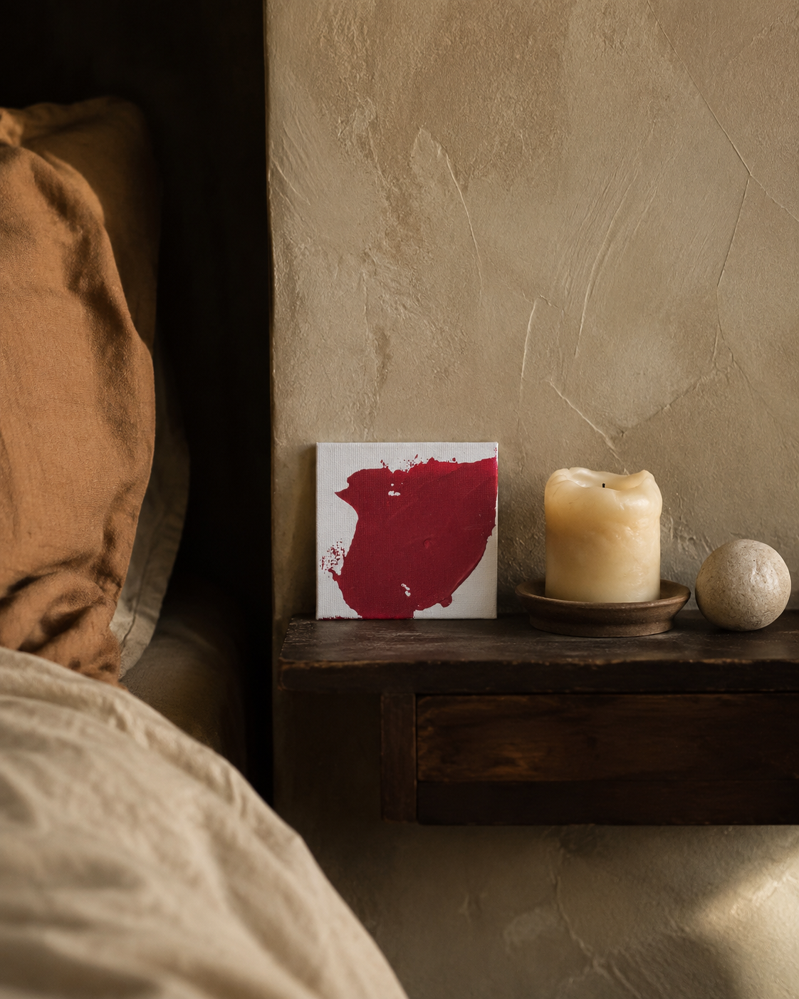 Handmade Artist Painting propped on a nightstand beside a candle in a warm plaster bedroom