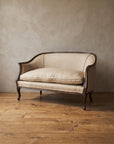 Vintage Bloomingdale's Trianon settee in oatmeal linen with a dark carved wood frame, against a plaster wall on a wide-plank wood floor