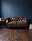 Leather chesterfield loveseat against a midnight blue plaster wall with a side table, books and tea